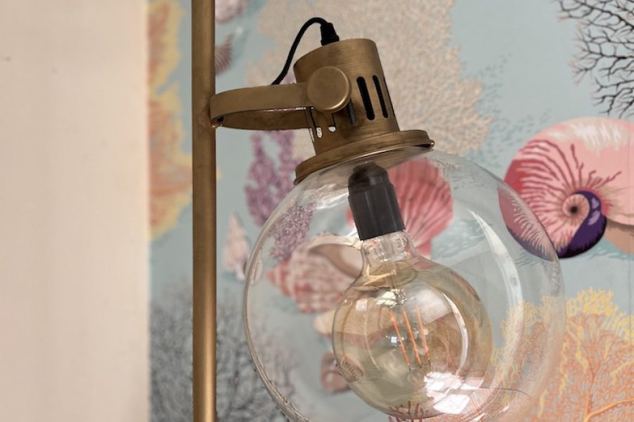Détail d'une lampe en laiton et d'un globe de verre devant un papier peint marin dans le Gite Le Herpin à Cancale dans la metairie du Vauhariot